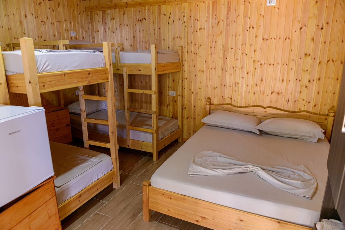 A room with bunk beds and a single bed, wooden walls, and a refrigerator.