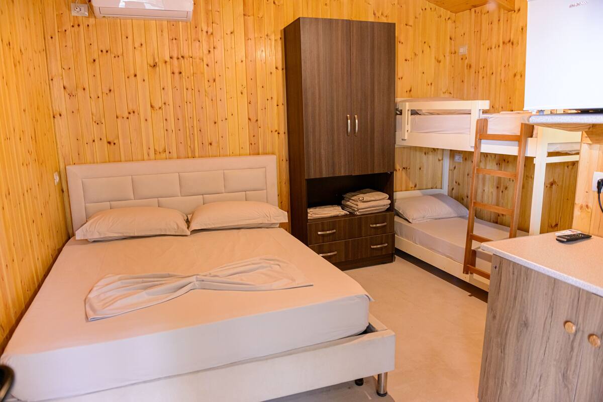 A wooden-paneled room with a bed, a wardrobe, and a bunk bed.