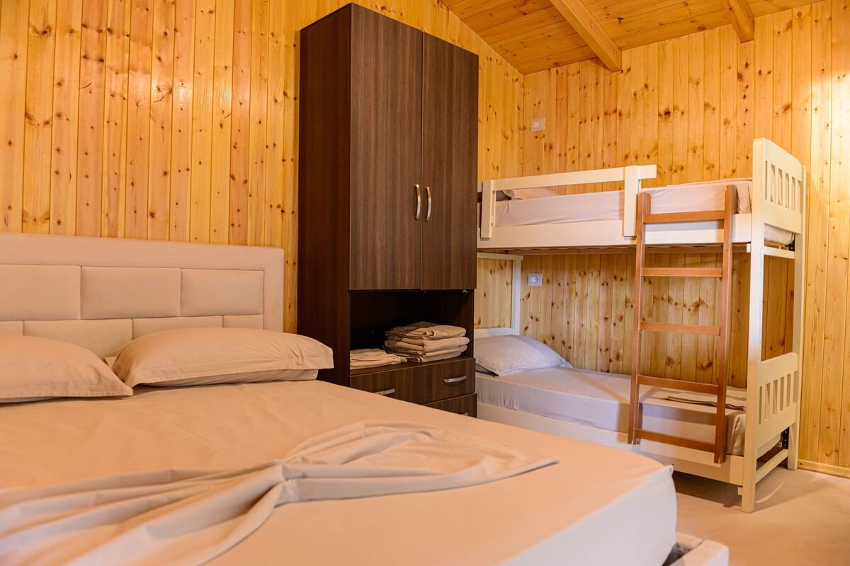 A wooden cabin room with bunk beds, a wardrobe, and a bedside table.