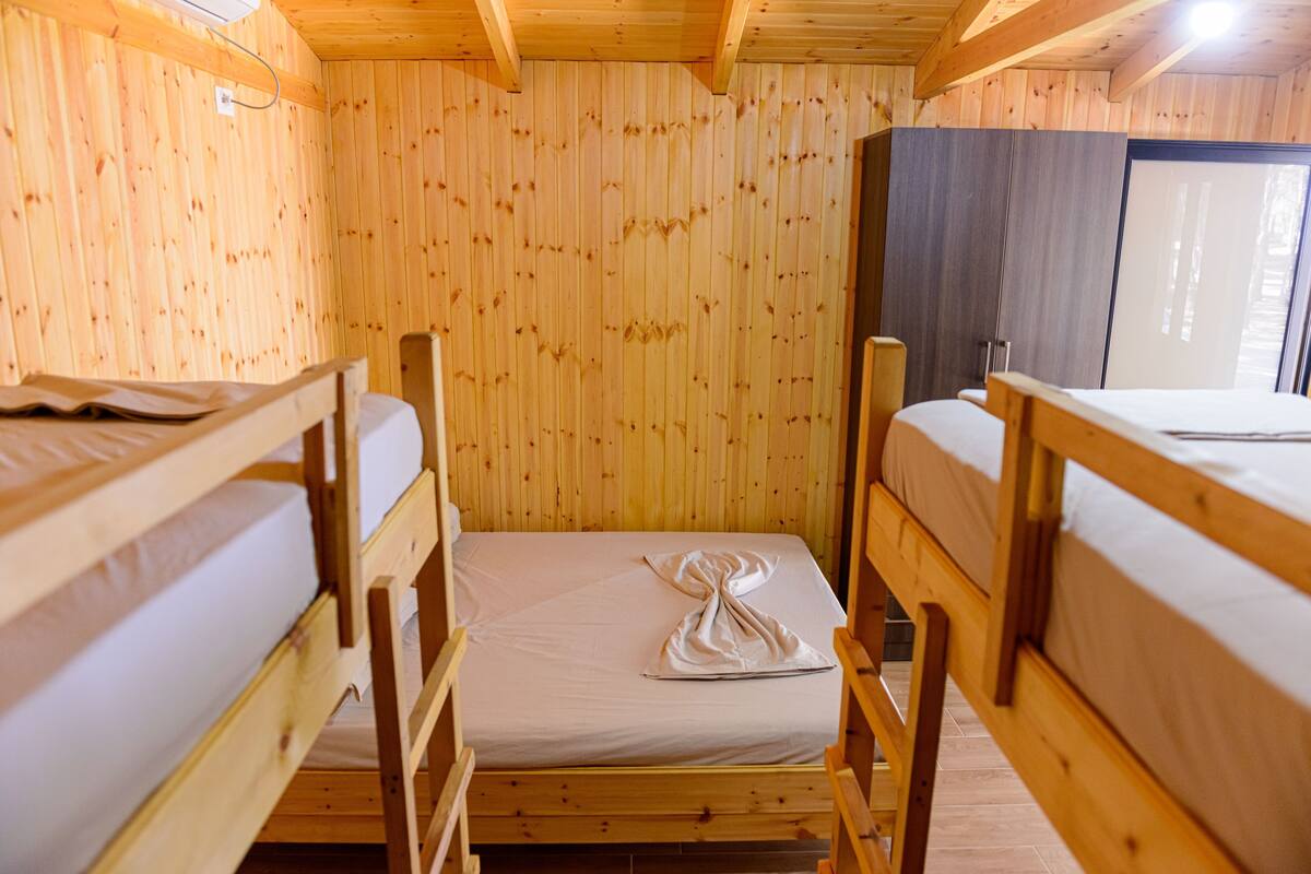 A wooden cabin room with bunk beds, a wardrobe, and a window.