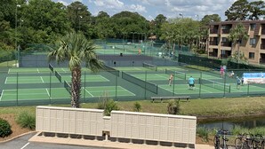 A tennis court surrounded by greenery and a water body.