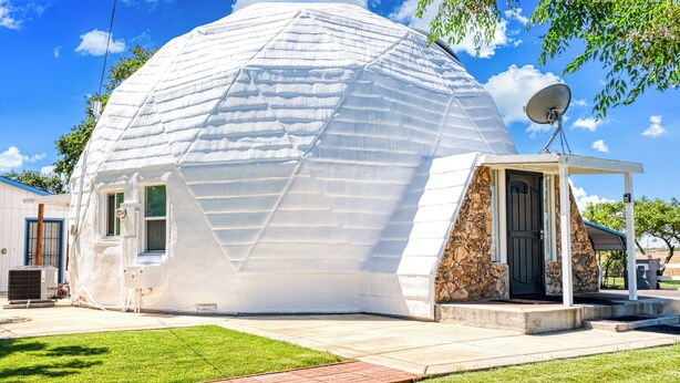 Een geodetische koepelvormige woning met een stenen gevel, een schotelantenne en een klein terras.