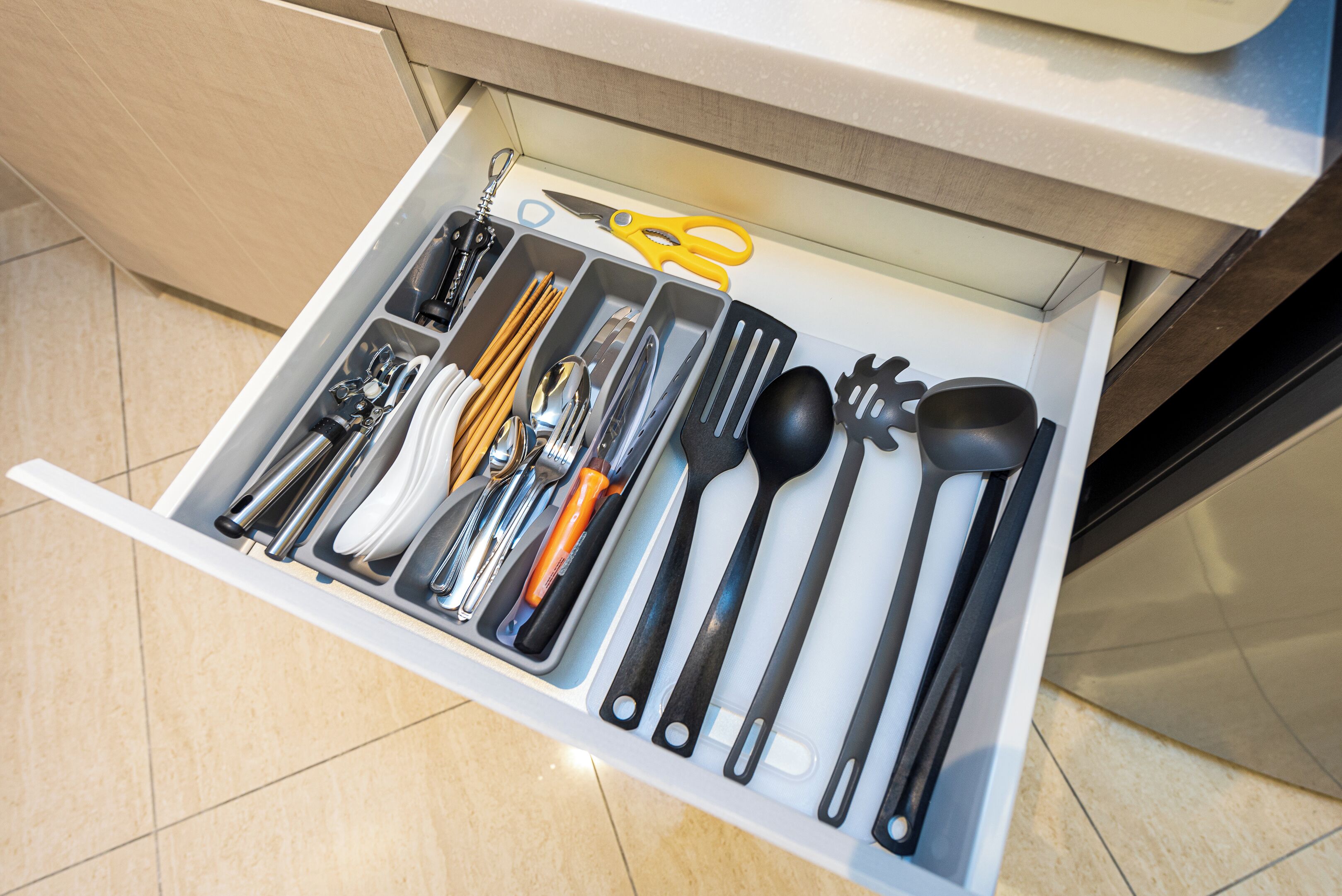 Un cajón con utensilios de cocina y un par de tijeras amarillas.