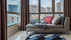 A modern living room with a sofa, a patterned rug, and a view of city buildings through large windows. - Dorsett Residences by BeYourHost (Kuala Lumpur)