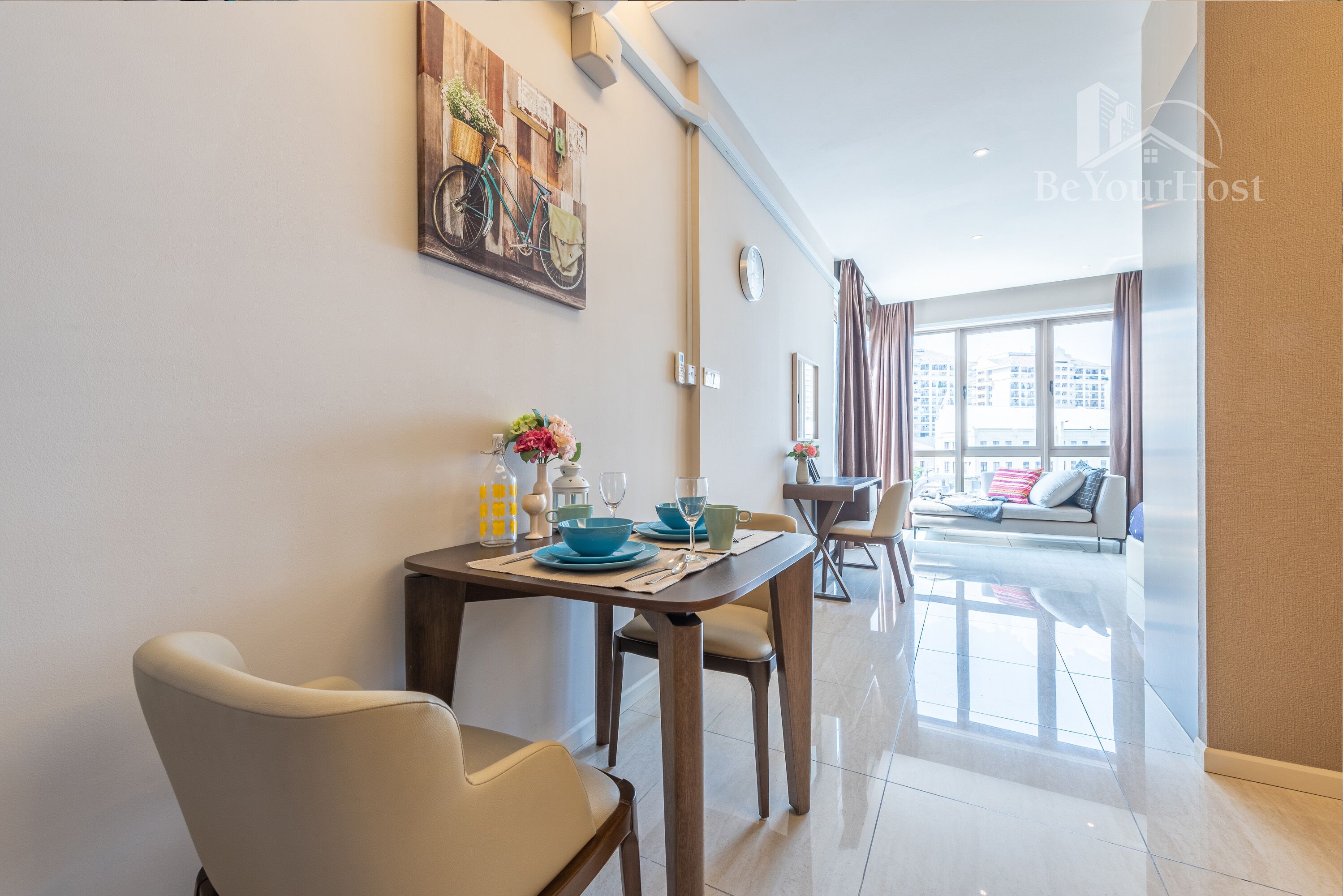 Uma sala de jantar moderna com uma mesa posta para dois, um quadro na parede e vista da cidade através de grandes janelas.