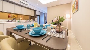 A modern kitchen with white cabinets, a dining area with blue plates and a vase of flowers, and a painting on the wall. - Dorsett Residences by BeYourHost (Kuala Lumpur)