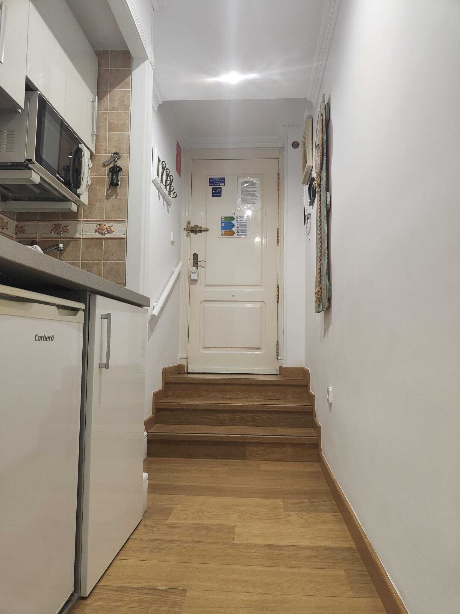 A narrow hallway with a kitchen on the left, a door at the end, and a staircase leading to another floor.