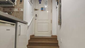 A narrow hallway with a kitchen on the left, a door at the end, and a staircase leading to another floor.