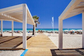 Une promenade en bois menant à une plage où l’on trouve des parasols et des gens.