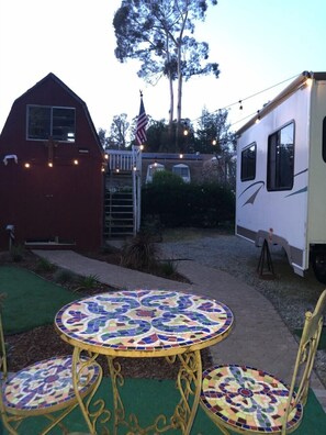 A patio area with a mosaic table and chairs, a red barn, and a white RV. - Fully sanitized with bbq & lawn, super soft linens, safe, country setting (Arroyo Grande)