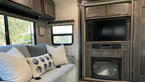 A cozy RV interior with a sofa, pillows, a television, and a fireplace. - Fully sanitized with bbq & lawn, super soft linens, safe, country setting (Arroyo Grande)