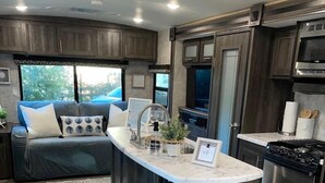 A modern RV kitchen with a central island, stainless steel appliances, and a cozy seating area with a view. - Fully sanitized with bbq & lawn, super soft linens, safe, country setting (Arroyo Grande)