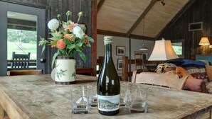 A rustic wooden table with a bottle of wine, glasses, and a vase of flowers in a rustic setting.