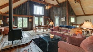 A cozy cabin interior with a stone fireplace, wooden beams, a dining area, and a living room with a sofa and lamps.
