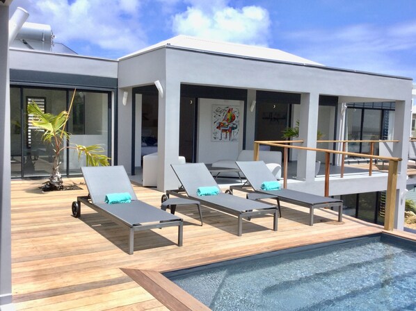 A modern outdoor pool area with lounge chairs and a wooden deck.