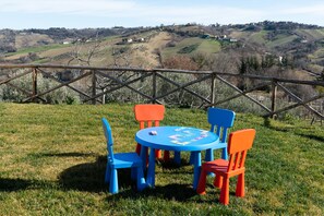 A table with chairs set outdoors on a grassy area, with a scenic view of hills and buildings in the background. - Casa Pace e Gioia - Restored farmhouse with private pool and amazing views (Tolentino)