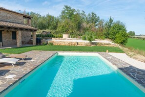 A rectangular swimming pool with stone tiles, surrounded by a stone patio and a grassy area. - Casa Pace e Gioia - Restored farmhouse with private pool and amazing views (Tolentino)