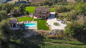 A two-story stone house with a swimming pool, surrounded by lush green fields and trees. - Casa Pace e Gioia - Restored farmhouse with private pool and amazing views (Tolentino)