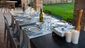 A table set for a meal outdoors with a view of a garden and stone wall. - Casa Pace e Gioia - Restored farmhouse with private pool and amazing views (Tolentino)