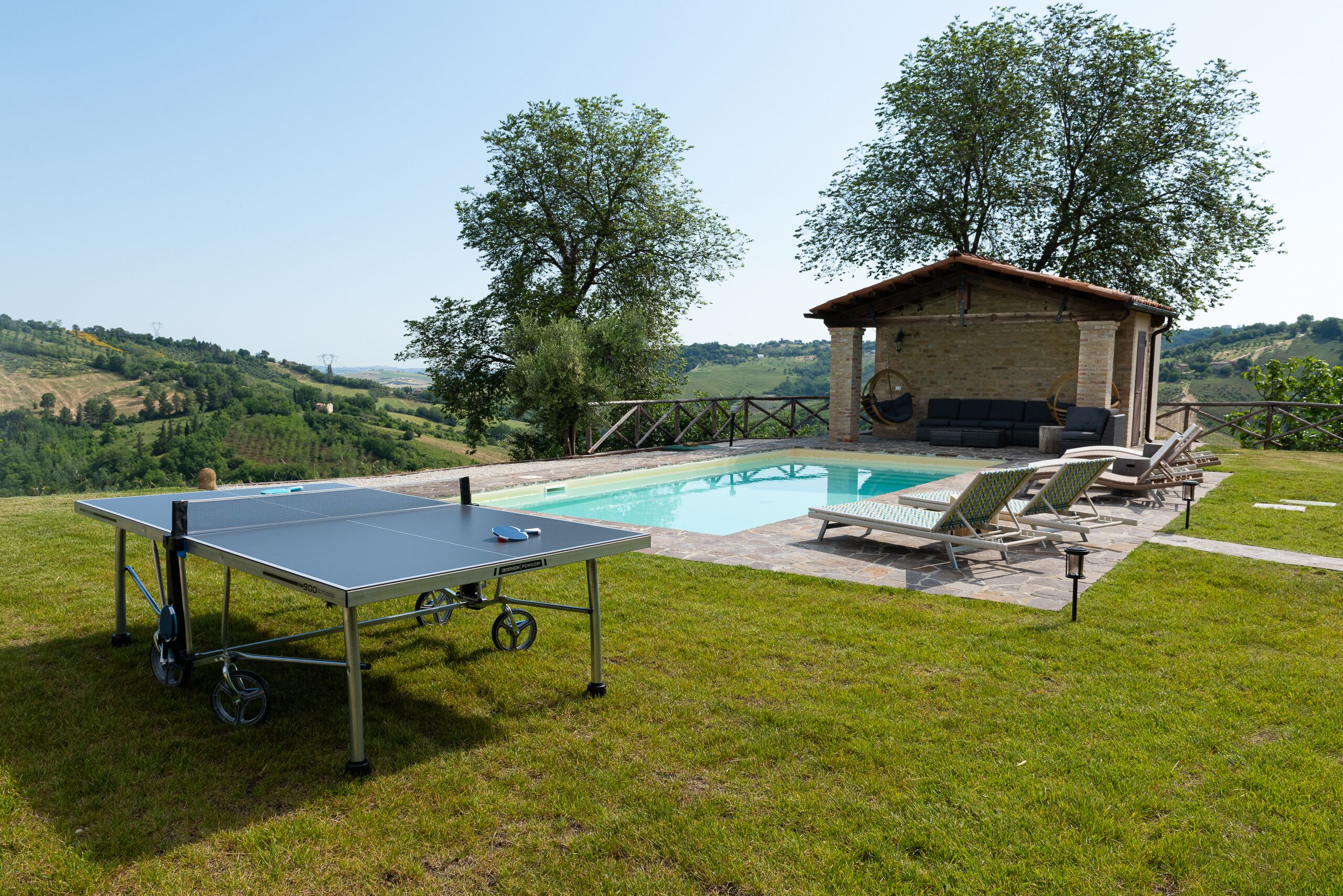 Un área de piscina con mesa de ping pong, sillas de descanso y un pequeño edificio con techo.