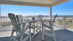 A covered outdoor seating area with Adirondack chairs and a table, overlooking a beach. - ☀️Spice Island-7BR Oceanfront-Saltwater Pool-Private Beach Access☀️ (Carolina Beach)