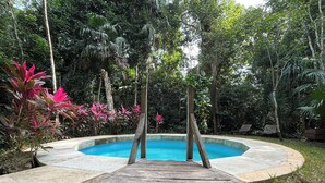 Une terrasse en bois mène à une piscine circulaire entourée d’une végétation luxuriante et de plantes tropicales.