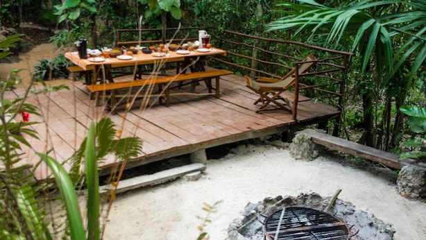 Une terrasse en bois avec une table dressée pour le repas, entourée d’une végétation luxuriante.