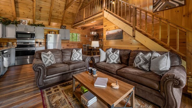 A cozy cabin interior with a wooden staircase, leather sofas, a dining area, and a kitchen with modern appliances. - Spectacular Mountain View! Hot Tub! Secluded! (Gatlinburg)