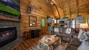 A cozy cabin interior with a stone fireplace, wooden walls, a living room with a sofa and coffee table, and a kitchen area. - Spectacular Mountain View! Hot Tub! Secluded! (Gatlinburg)