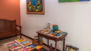 A room with a wooden bench, a table with books and a vase, and a painting on the wall. - Ecotel (Managua)
