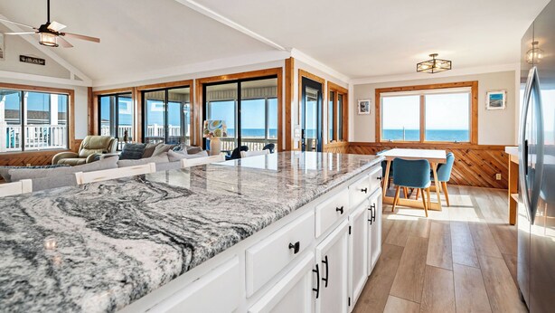A spacious kitchen with a large island, wooden accents, and large windows offering ocean views. - A Bella Vista: Coastal Cool Oceanfront Home with Ramp (Oak Island)
