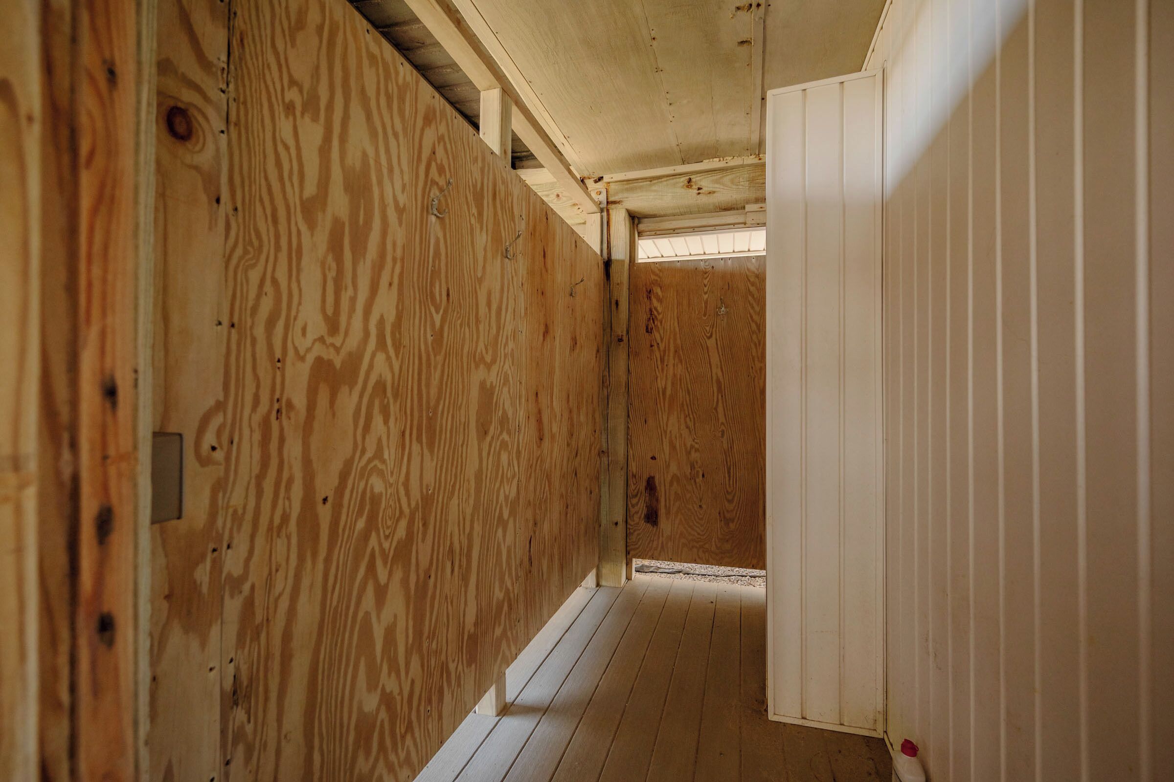 Un couloir étroit aux murs en bois, avec une porte blanche au fond.