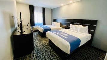 Habitación de hotel con dos camas, un escritorio, un televisor y una ventana con cortinas.