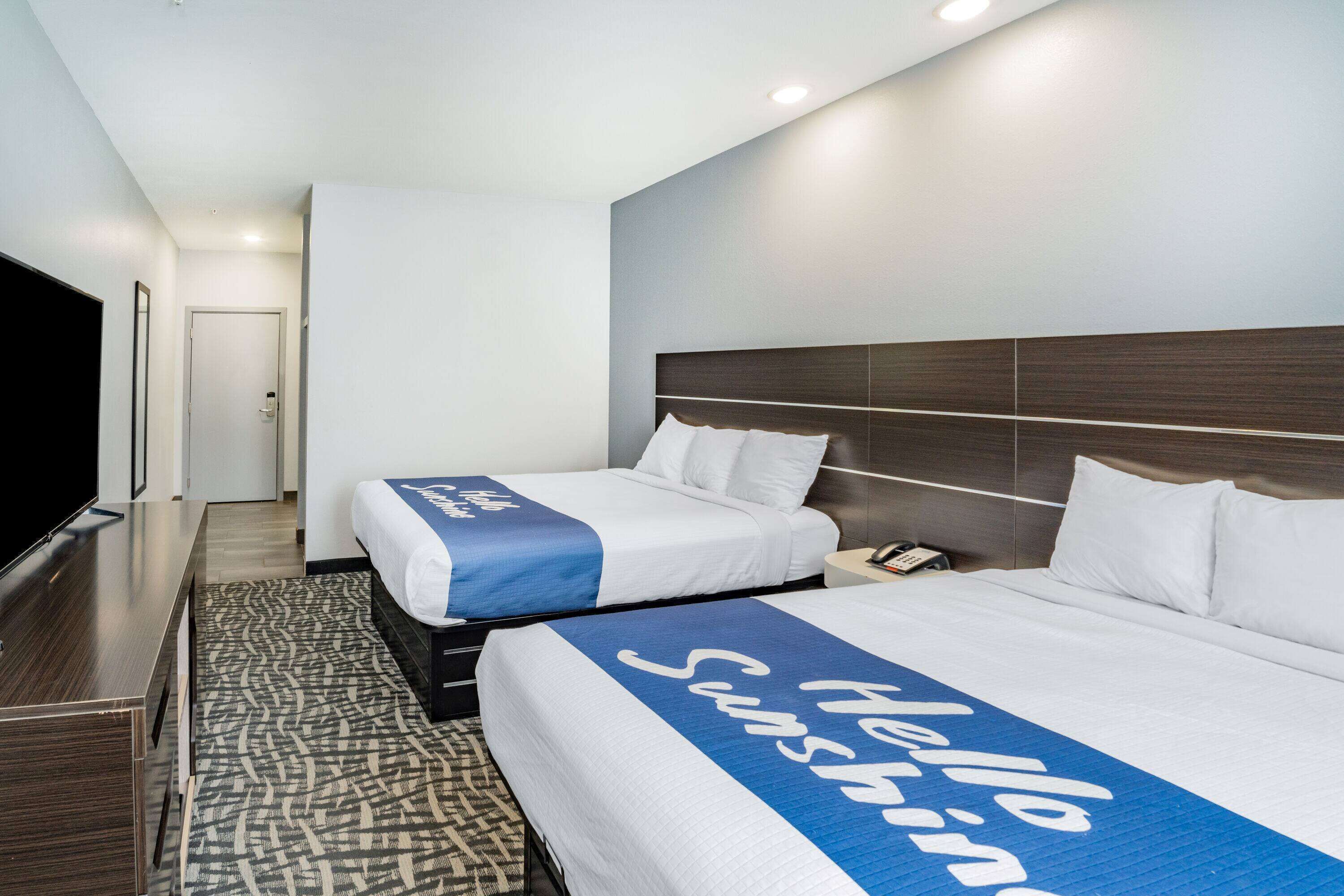 Ein Hotelzimmer mit zwei Betten, einem Flachbildfernseher, einem Schreibtisch und einem gemusterten Teppich.