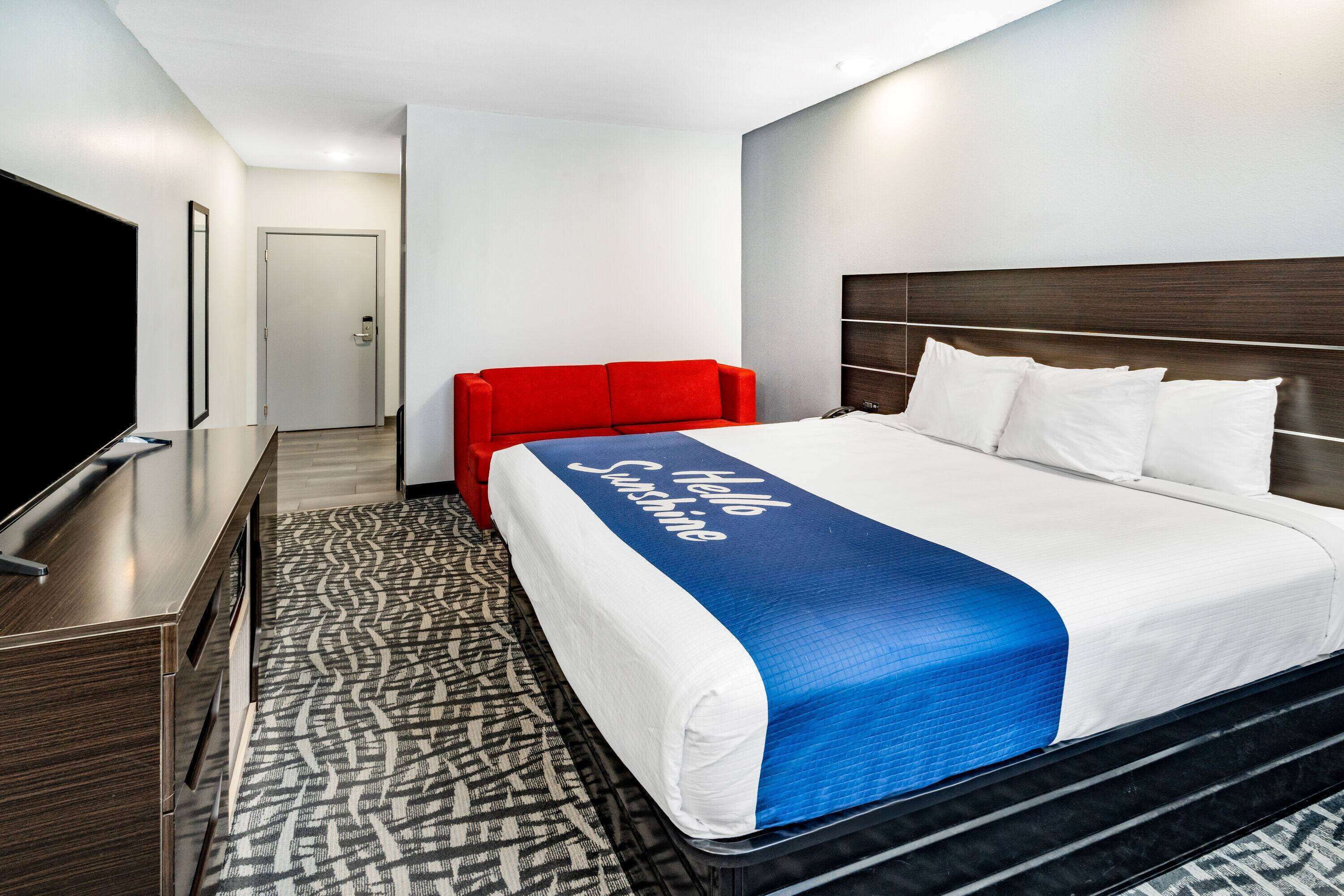 Quarto de hotel com uma cama grande, um sofá vermelho, uma televisão de tela plana e um tapete estampado.