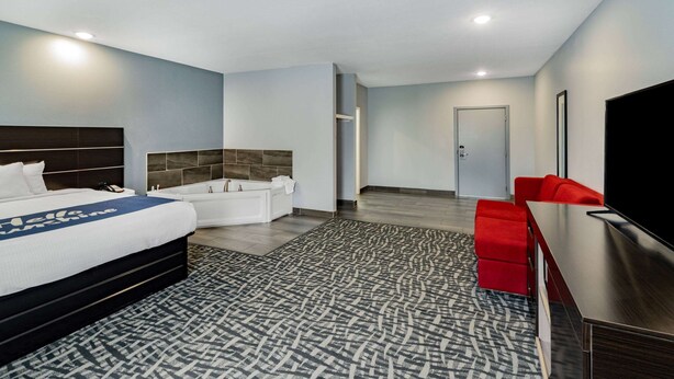 A modern hotel room with a large bed, a separate bathroom, a flat-screen TV, and a red sofa.