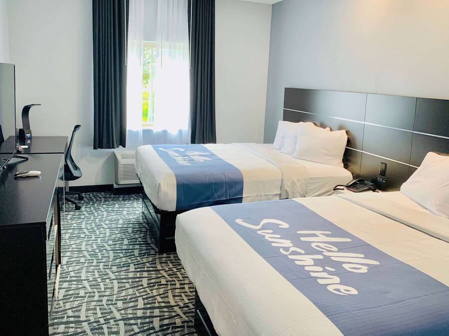 Een hotelkamer met twee bedden, een bureau met een computer, een stoel en een groot raam met gordijnen.