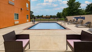 A swimming pool with lounge chairs, a lifeguard sign, and a building in the background.