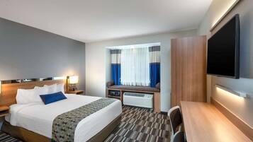 Une chambre d’hôtel avec un grand lit, des tables de chevet, un bureau, un téléviseur à écran plat et une fenêtre avec des rideaux.