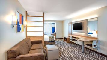 A hotel room with a sofa, a bed, a desk, a TV, and a window with curtains.