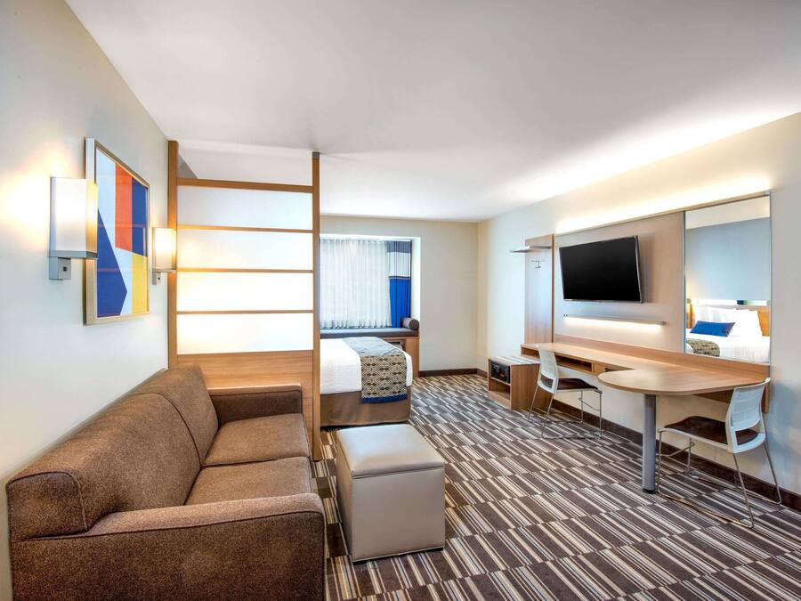 Ein Hotelzimmer mit Sofa, Bett, Schreibtisch, Fernseher und einem Fenster mit Vorhängen.