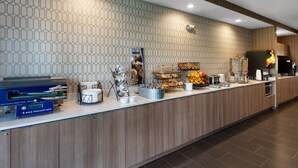 A breakfast bar with a self-serve pancake station, a variety of pastries, and a coffee machine.