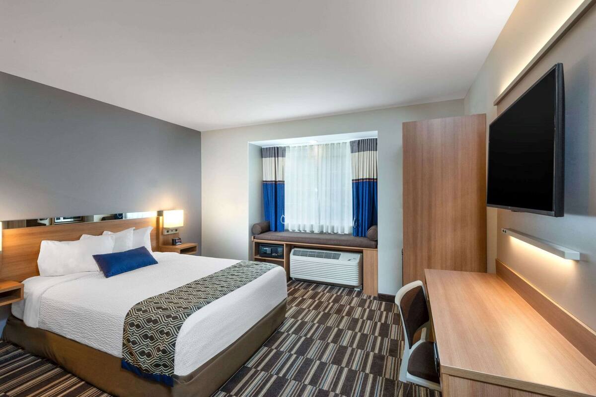 A hotel room with a bed, bedside tables, a desk, a flat-screen TV, and a window with curtains.