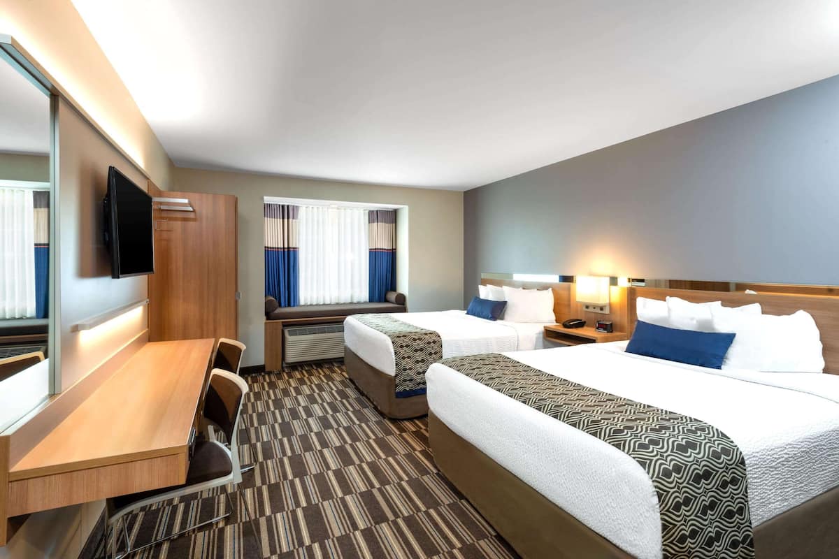 A hotel room with two beds, a desk, a TV, and a window with curtains.