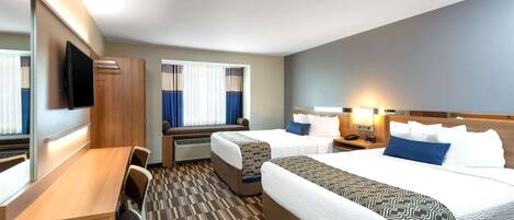 Une chambre d’hôtel avec deux lits, un bureau, une télévision et une fenêtre avec des rideaux.