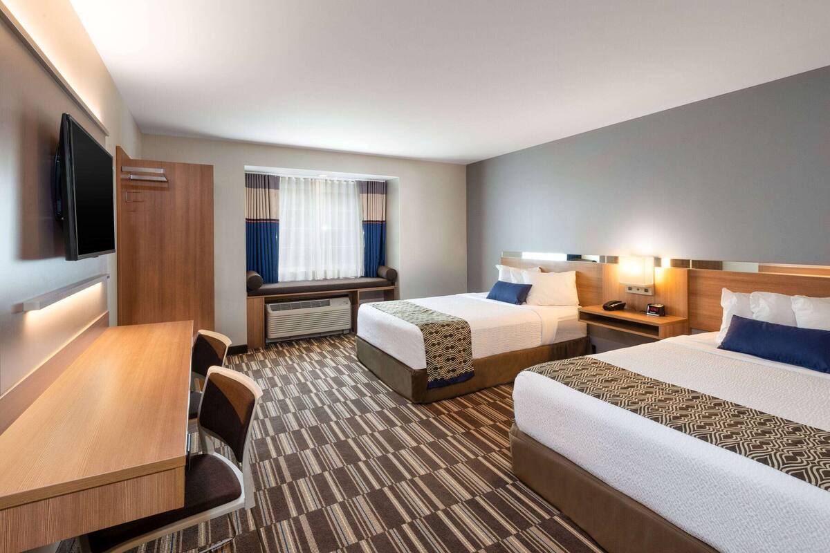 A hotel room with two beds, a desk, a chair, a TV, and a window with curtains.