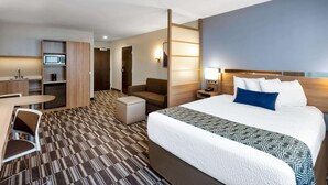 A hotel room with a large bed, a desk, a chair, a sofa, a small table, a microwave, a coffee maker, and a TV.