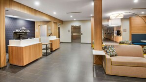 A modern hotel lobby with a reception desk, seating area, and a visible elevator.