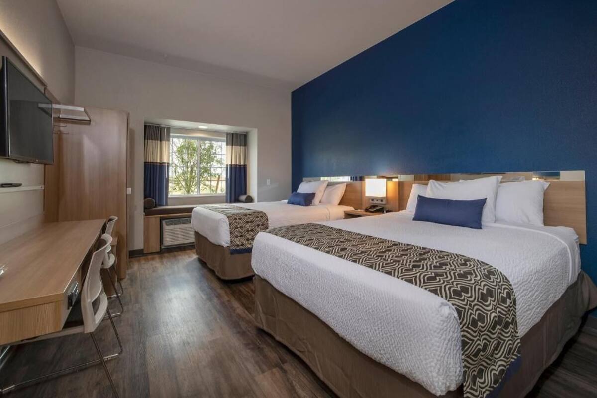 A hotel room with two beds, a desk, a TV, and a window with curtains.