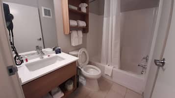 A bathroom with a sink, toilet, and shower. There is a towel rack above the toilet and a shelf with towels.